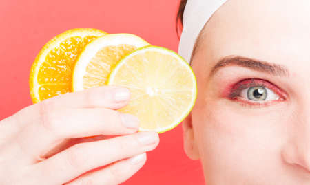 Female eye in closeup with citrus in hand as vitamin and vitality concept on red backgroundの写真素材