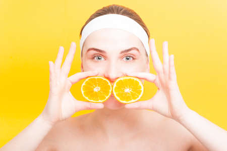 Attractive woman with two slices of orange fruit on her mouth as nutritive skincare concept on yellow backgroundの写真素材