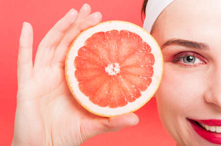 Closeup woman with smooth skin holding a slice of grapefruit and smiling on red backgroundの写真素材