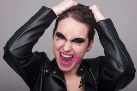 Rock style girl in an aggressive posture posing with dirty make up on grey backgroundの写真素材