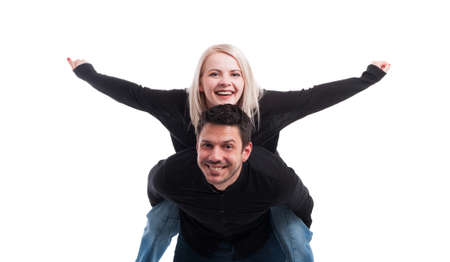 Young man giving piggyback ride to woman who stands with arms outstretched on white backgroundの写真素材