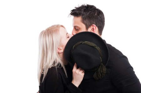 Young couple hiding behind hat and kissing on white background with text space