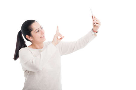 Cheerful lady taking a selfie and showing peace sign on white studio background
