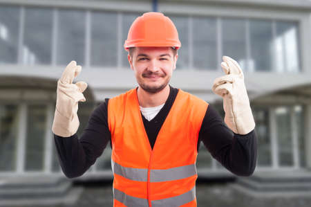 Cheerful architect with fingers crossed from both hands feeling lucky in front of buildingの写真素材