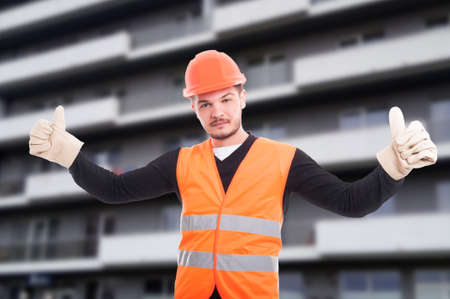Successful builder shows double like sign with both hands on construction siteの写真素材