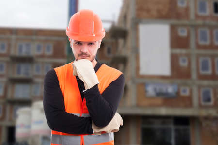 Pensive male engineer outside in front of building wearing protection equipmentの写真素材