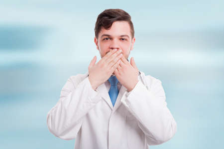 Portrait of doctor making silence or speak no evil gesture isolated on blue backgroundの写真素材