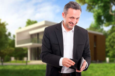 Successful realtor counting money from his wallet outdoors in front of the houseの写真素材