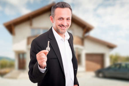 Young realtor offering house keys as real estate selling conceptの写真素材