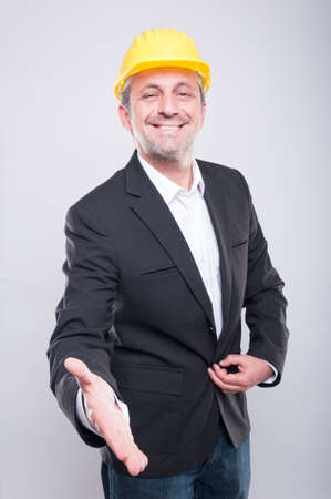 Handsome contractor wearing helmet offering hand shake and smiling on grey backgroundの写真素材