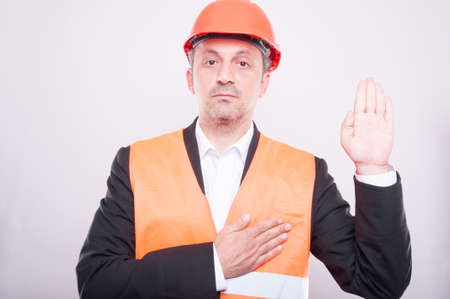 Engineer wearing hardhat making oath gesture wearing reflective vest on grey background
