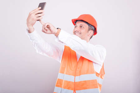 Foreman wearing reflective vest making selfie and smiling  on grey backgroundの写真素材