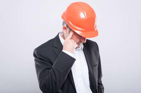 Foreman wearing hardhat making thinking gesture looking down on grey backgroundの写真素材