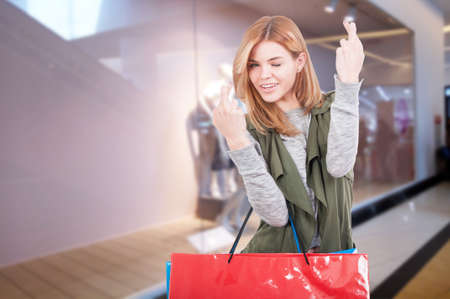 Fashion woman with shopping bags in the mall buying some gifts and holding fingers crossedの写真素材