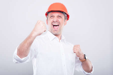 Portrait of architect wearing hardhat making winner gesture holding fists on grey backgroundの写真素材