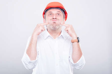 Portrait of contractor wearing making silly gesture pointing cheeks on grey backgroundの写真素材