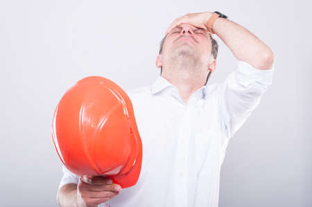 Portrait of architect holding hardhat making head ache gesture on grey backgroundの写真素材