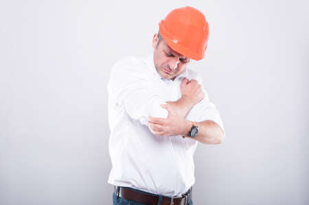 Portrait of contractor wearing hardhat holding elbow like hurting on grey backgroundの写真素材