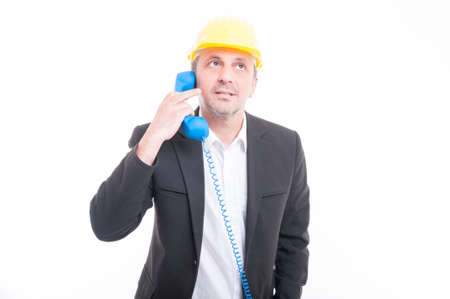 Portrait of architect talking on blue big telephone receiver wearing yellow hardhat isolated on white backgroundの写真素材