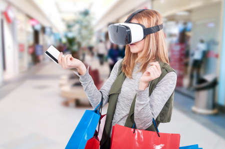 Female shopper experiencing virtual reality equipment video and using credit card as e-commerce...