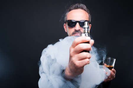 Stylish man with a glass of whiskey and electronic cigarette as luxury and high life concept