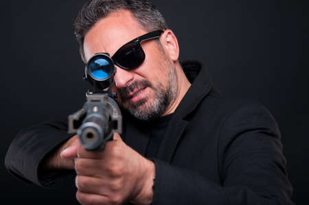 Mafia murderer aiming his weapon at the camera looking dangerous on black backgroundの写真素材