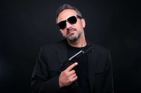 Gangster hitman assassin holding a gun over dark background looking dangerousの写真素材