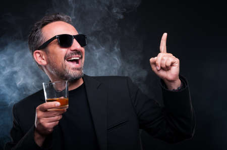 Cheerful rich male with a glass of whiskey dancing on dark background as luxury and classy lifestyle conceptの写真素材