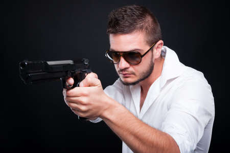 Handsome mafia member pointing with gun at his target on dark backgroundの写真素材