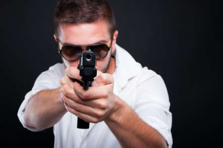 Gangster killer with a rough look aiming at you with automatic gun isolated on black backgroundの写真素材