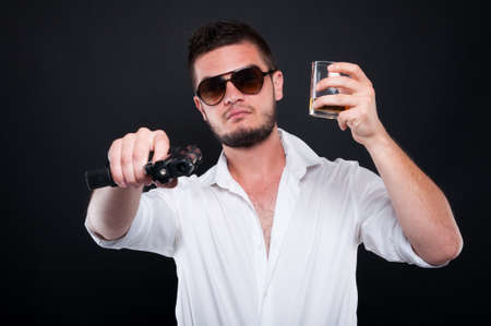 Mafia boss aiming gun or pistol at you while drinking whiskey on dark backgroundの写真素材