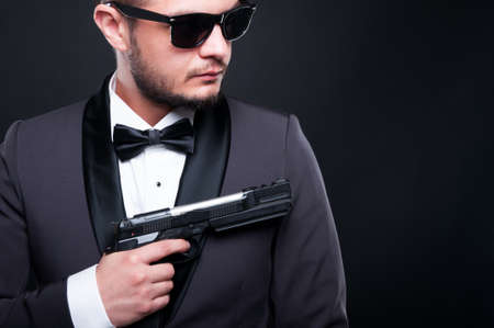 Handsome mafia member or secret agent with armed revolver on black background with copyspaceの写真素材