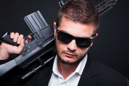 Closeup portrait of male gangster with automatic weapon looking at the camera on dark backgroundの写真素材
