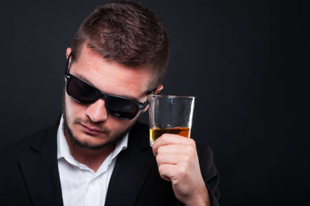 Portrait of young classy male with glass of whiskey in close-up view thinking at somethingの写真素材