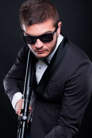 Mafia guy with armed rifle preparing to shoot isolated on black background