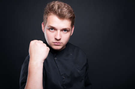 Aggressive cook holding up his fist arguing with somebody on dark backgroundの写真素材