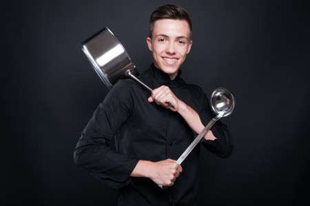 Cheerful chef with kitchen ustensils getting ready to prepare a good meal on dark backgroundの写真素材