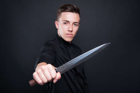 Professional cook holding knife at the camera with serious expression on his faceの写真素材