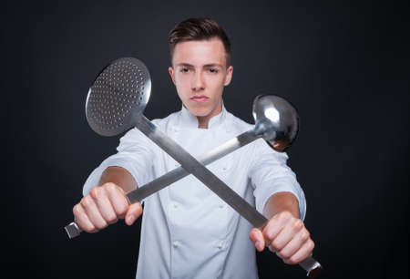 Portrait of chef holding crossed ladle and skimmer isolated on black backgroundの写真素材