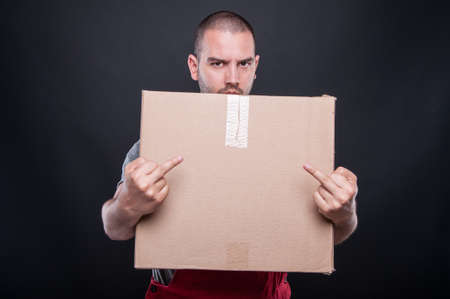 Angry mover man holding box showing double obscene gesture on black backgroundの写真素材