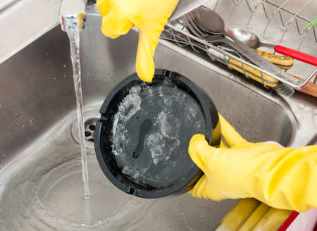 Housemaid holding dirty ashtray in the kitchen sink and cleaning it in close-upの写真素材