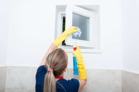 Young woman wiping small window at home and doing general cleaningの写真素材