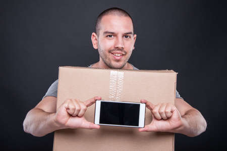 Mover man holding box showing smartphone blank screen on black background
