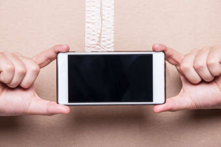 Close-up of man showing blank smartphone screen with cardboard box on background with copypsace advertising areaの写真素材