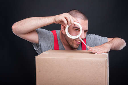 Mover guy packing box with duct tape being playful and smiling on black backgroundの写真素材