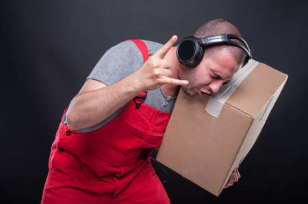 Mover guy holding box gesturing rock music listening to headphones on black backgroundの写真素材