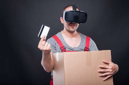 Mover guy holding box and credit card wearing vr glasses on black background with copy text spaceの写真素材