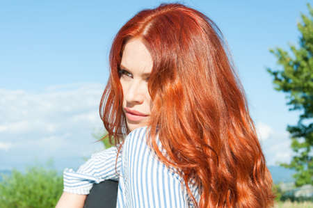 Young pretty redhead girl in summer meadow resting outsideの写真素材
