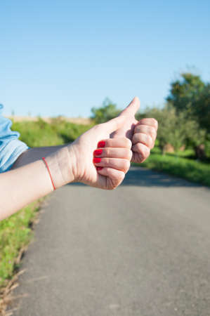 Young couple hitchhiking with thumb up gesture on countryside road in closeup