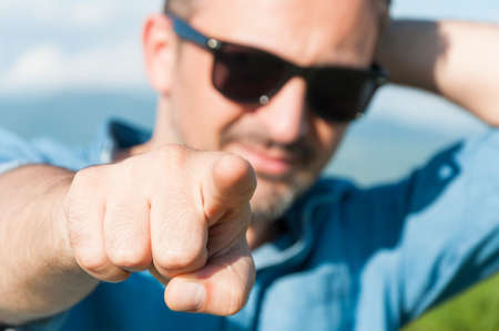 Closeup of relaxed handsome guy pointing you with finger while spending time on nature